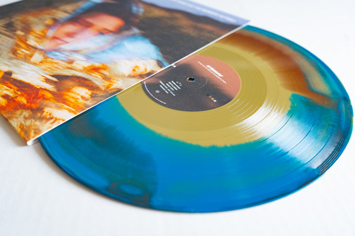 A limited edition marbled Gold/Blue/Brown Vinyl LP by Shoreline is partially out of its sleeve, featuring a blurred, colorful image of a person. The brown center label with white text makes it perfect for any album presale.