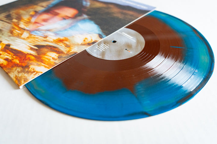 A close-up of Shoreline’s Gold/Blue/Brown marbled Vinyl LP, partially in sleeve. The limited edition features a blurred portrait cover with warm-toned patterns—an eye-catching addition to any album presale collection.