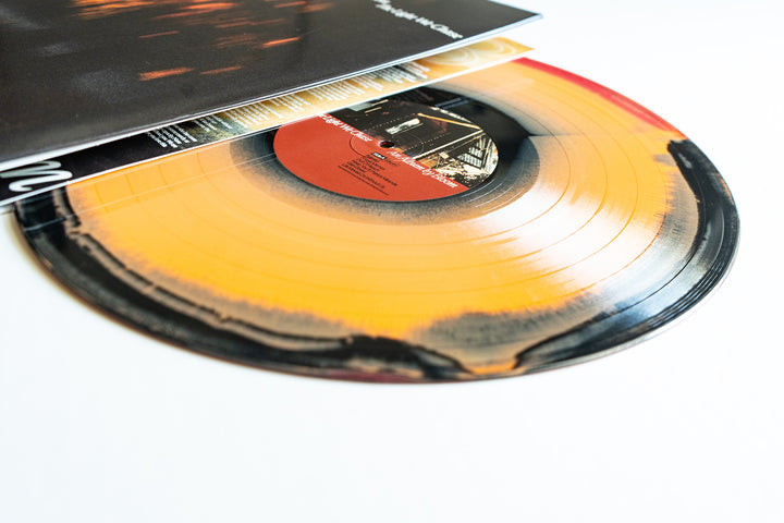 A yellow and black Bloom "The Light We Chase" vinyl partially slides out of its cover, revealing a vibrant pattern. The white background highlights the unique design of this limited edition album.