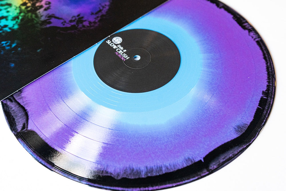 A vibrant vinyl record from Slow Crush, featuring a blue center fading into purple and black edges, peeks from a colorful album cover—ideal for presale before the official shipping date.