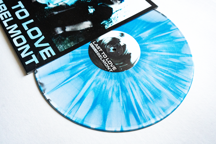A Blue White Black splatter LP partly out of its sleeve, featuring the bold text LAST TO LOVE and Belmont. The vinyl label matches the eye-catching album art—an essential collectors item or presale pick for Belmont fans.