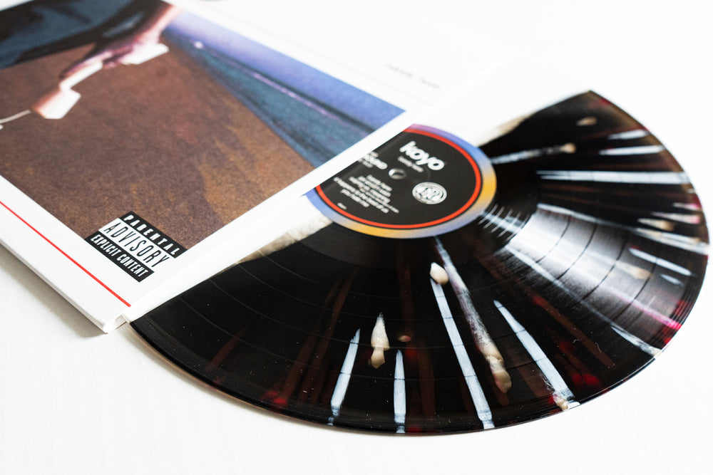 A KOYO vinyl LP partially pulled from its album cover reveals a unique Barely Here vinyl design, a parental advisory explicit content label, and cover art featuring a beach scene.