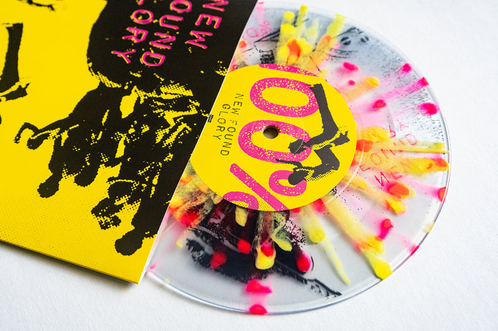 A clear vinyl record with neon yellow and pink splashes, partially covered by a bright yellow and black sleeve with bold New Found Glory text and abstract art.