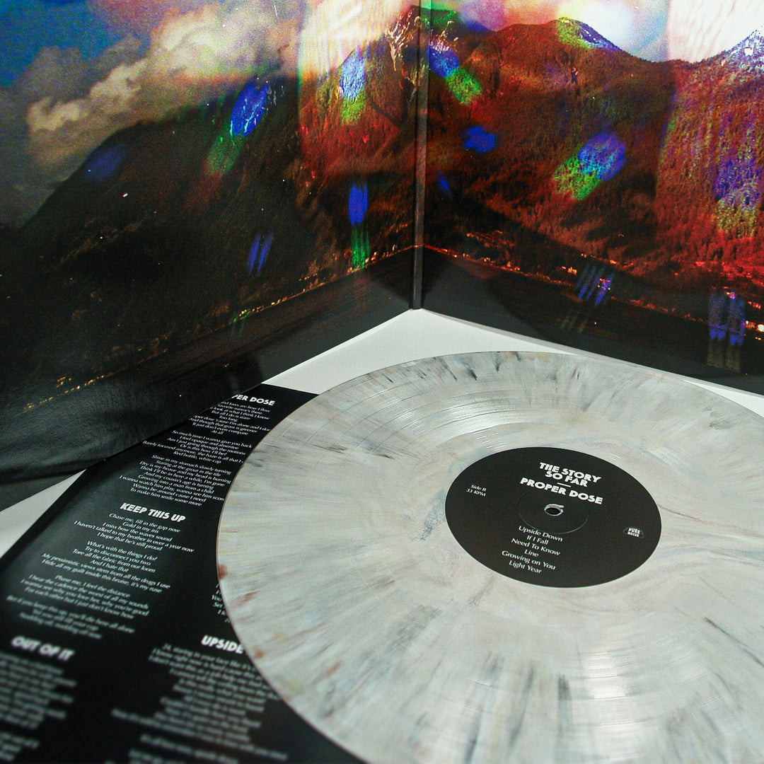 A marbled gray Proper Dose vinyl by The Story So Far rests on its open album cover, displaying a vivid mountain landscape and tracklist—an exclusive collector’s item for fans.