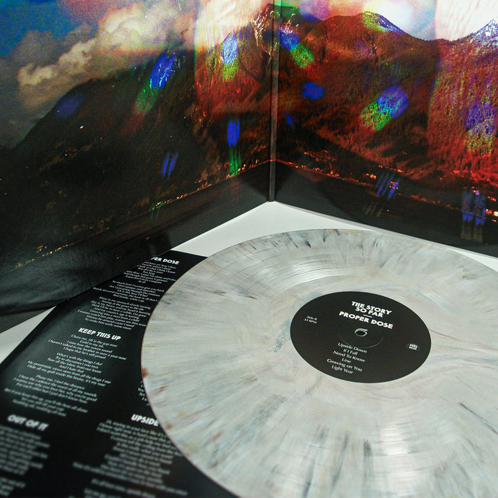 A marbled gray Proper Dose vinyl by The Story So Far rests on its open album cover, displaying a vivid mountain landscape and tracklist—an exclusive collector’s item for fans.