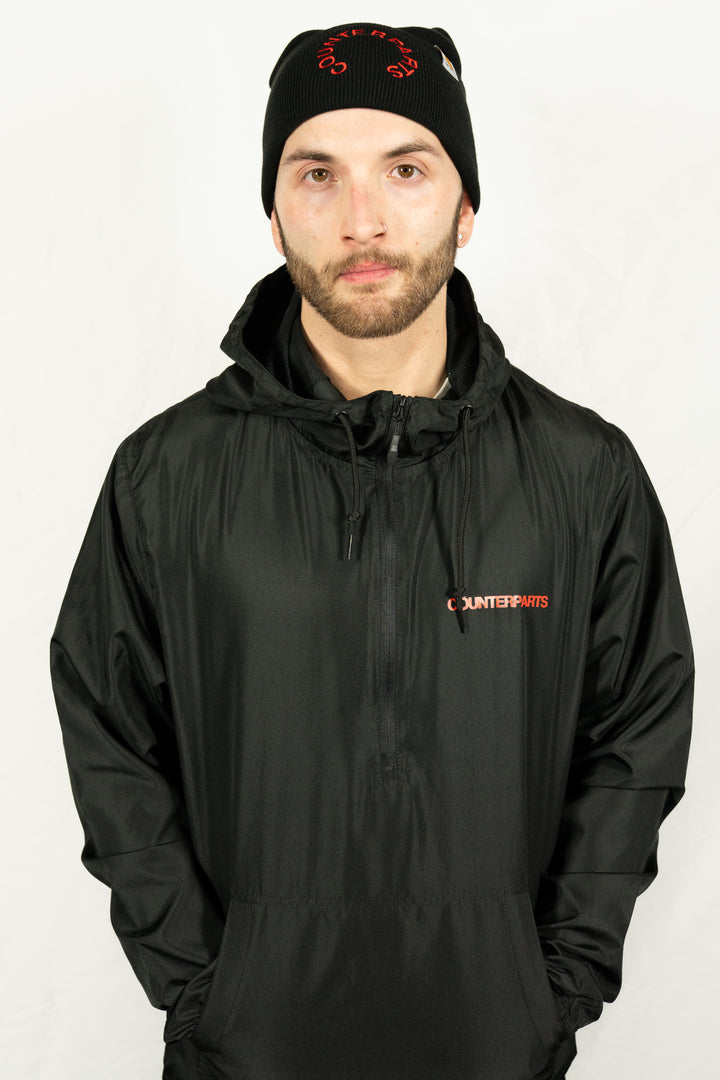 A man stands before a plain white background, wearing a black Counterparts unisex jacket with the brand's name on it and a black beanie with red lettering.