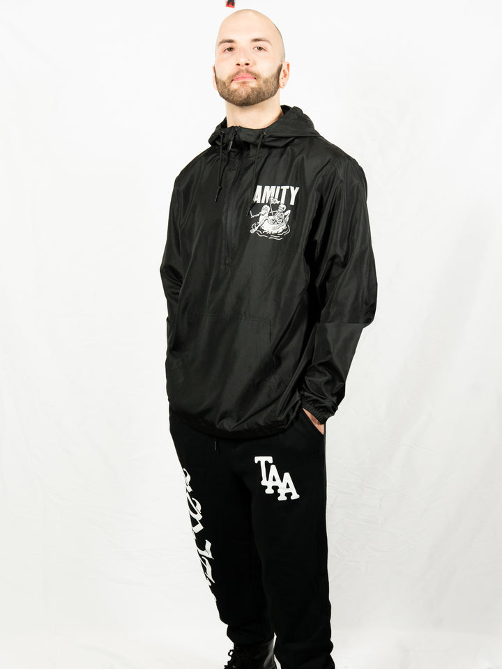 A person with a trimmed beard stands against a white background, wearing a black jacket with The Amity Affliction branding and graphic, and IND20PNT midweight fleece sweatpants by Independent Trading Co with bold white text and TAA initials on the leg.