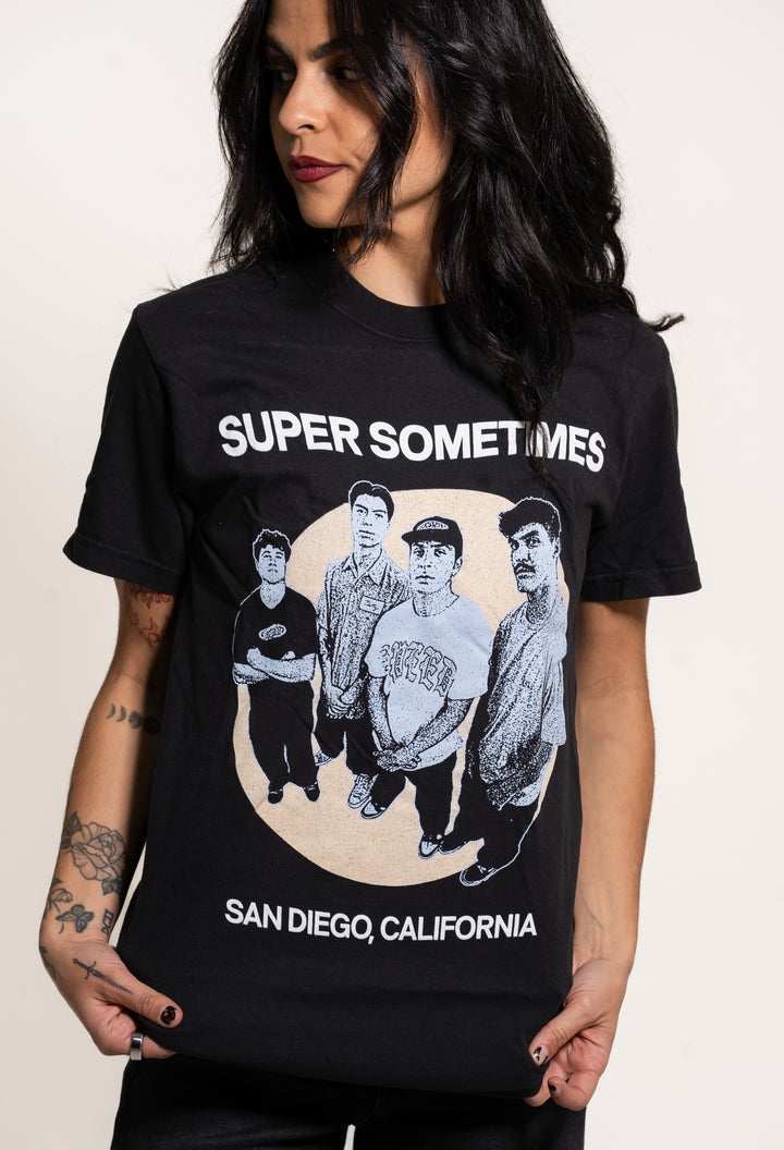 A woman with long dark hair wears a black Super Sometimes T-shirt featuring a photo of four men, with "SUPER SOMETIMES" above and "SAN DIEGO, CALIFORNIA" below the image.