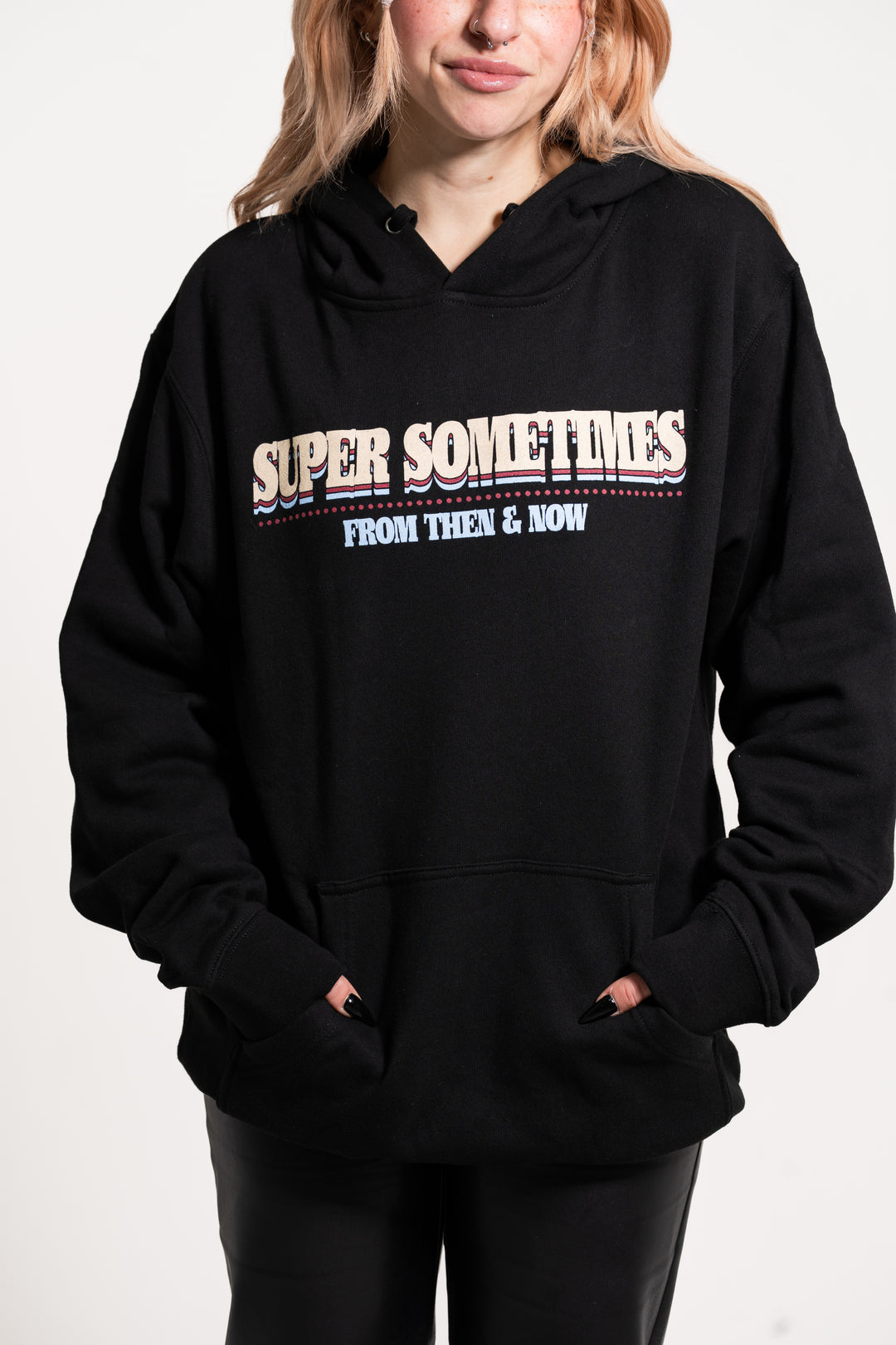 A person wearing a black Super Sometimes hoodie with "SUPER SOMETIMES FROM THEN & NOW" on the front, standing against a plain white background.