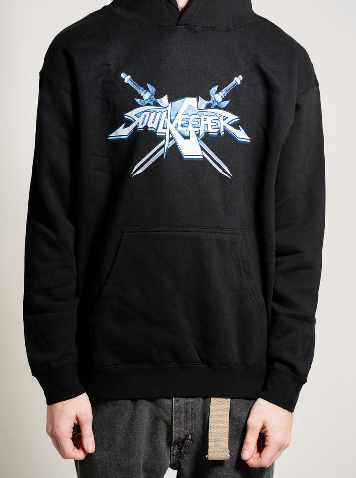 A person wearing a Soulkeeper black midweight pullover hoodie featuring a blue graphic logo with crossed swords on the chest, paired with dark jeans. The person's face is not visible.