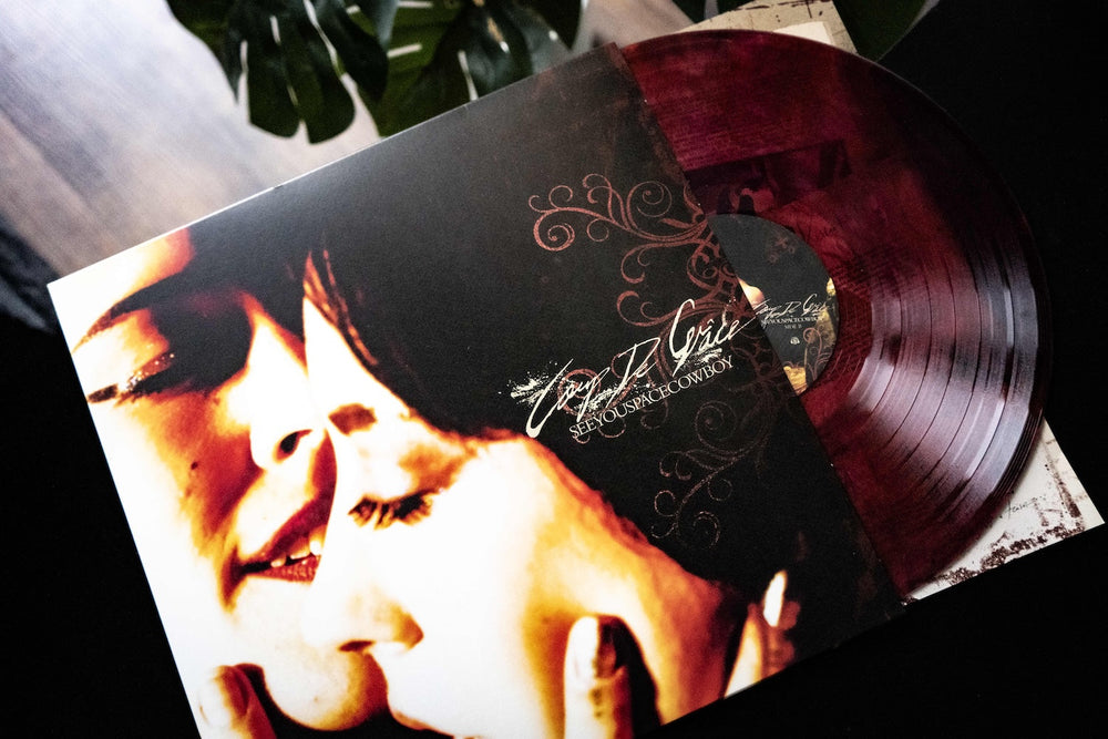 A maroon vinyl record partially pulled from its album cover, featuring a close-up of two faces. Allow Us To Set The Scene: the album is Sex, Love & Rock N Roll by SeeYouSpaceCowboy.