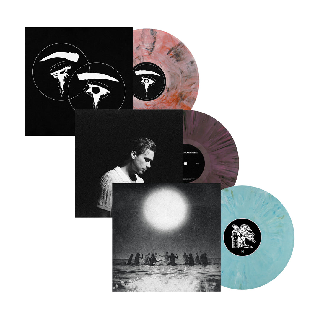 Three colored vinyl records—pink-black, purple-black, and blue-white—partially in black sleeves with unique designs, are displayed with two square Seahaven album covers: one showing a portrait and the other a sunlit scene.