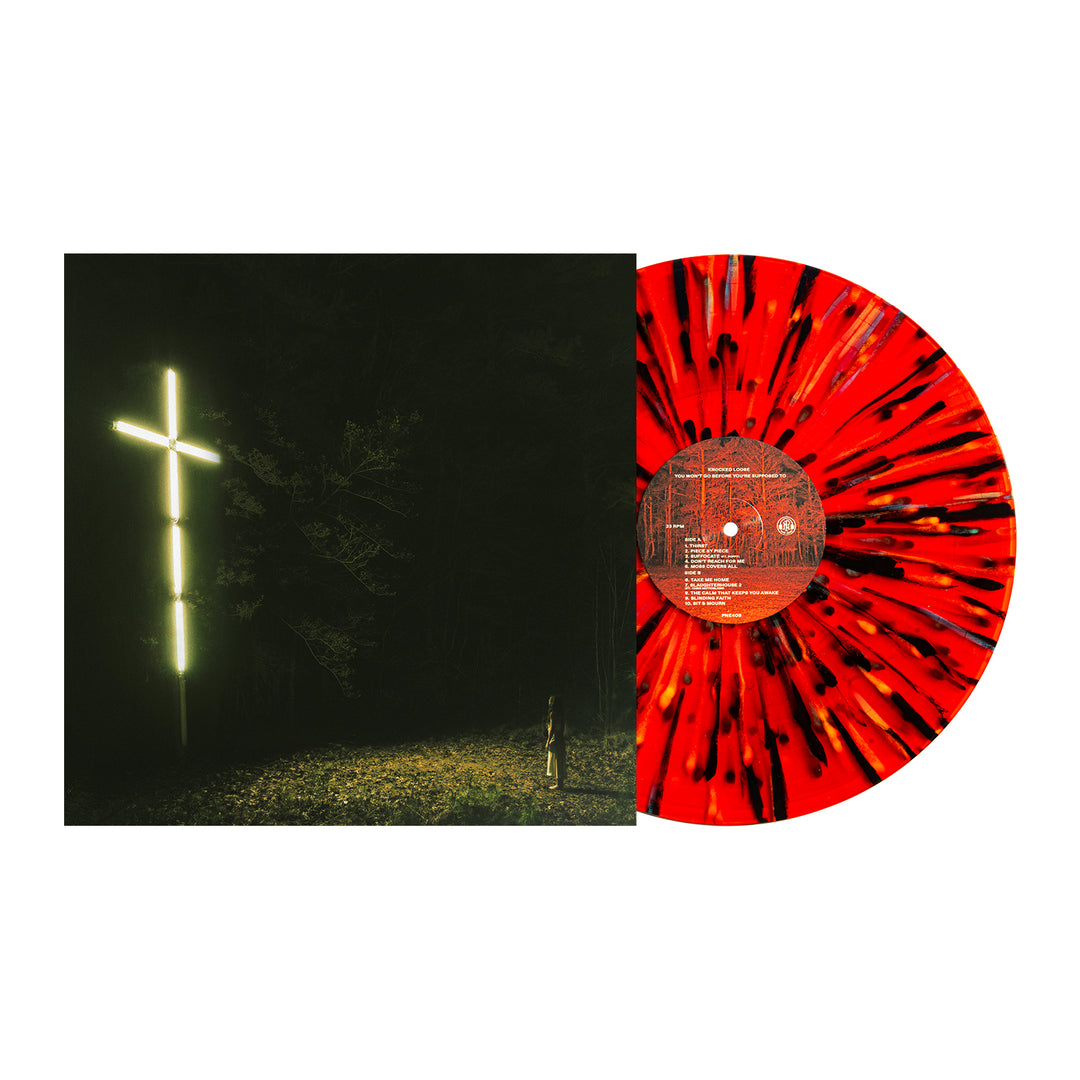 A limited edition Knocked Loose vinyl with a blood red and black splatter design rests beside its album cover, which shows a glowing cross in a dark forest illuminated by a beam of light.