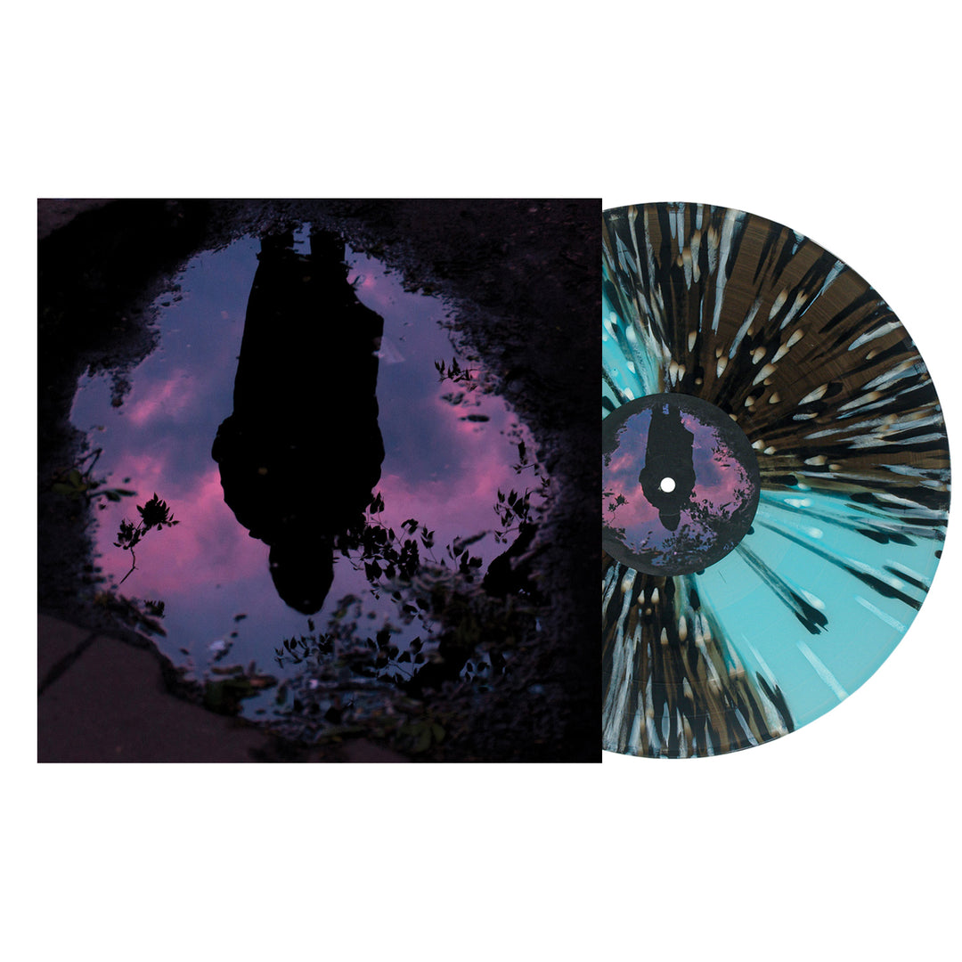 A Slow Crush vinyl record with black, white, and aqua splatter is partially pulled from an album cover featuring a silhouette reflected in a sunset puddle under purple and pink clouds.