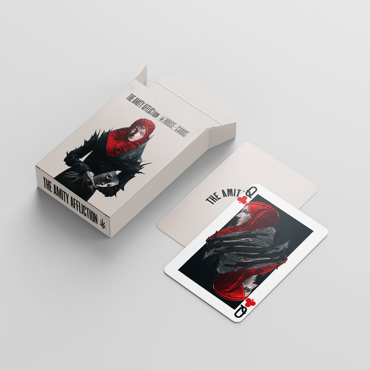A box of The Amity Affliction playing cards displays gothic art of a woman in a red hood. Next to the box are a Queen of Hearts card and a blank card.