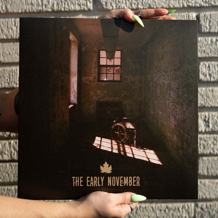 A person with long, green-painted nails holds The Early November’s Lavender Eco Mix Vinyl LP, featuring a cover of a dim room with a wheelchair and window. The album title sits above a maple leaf logo on this special presale edition.