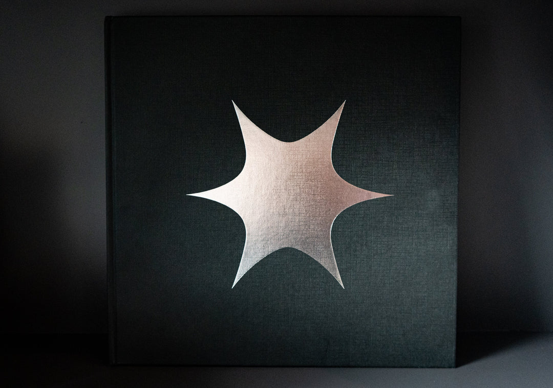 A dark deluxe book by The Story So Far featuring a large metallic eight-pointed starburst on the front cover, set against a plain background—reflecting the mysterious allure of “I Want To Disappear.”.