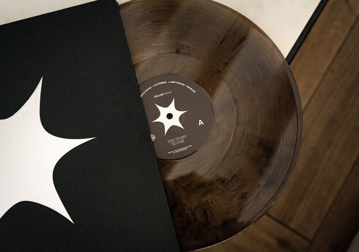 A brown marbled vinyl LP by The Story So Far partially slides from a black sleeve with a white starburst, labeled I Want To Disappear, displayed on a wood and white background.