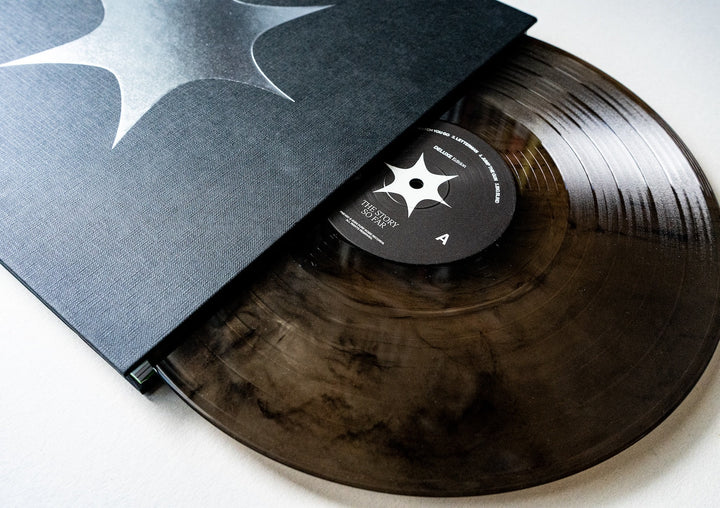 A close-up of The Story So Far’s smoky, translucent black Vinyl LP—partially slid from a matching black sleeve adorned with a white abstract star. The label echoes the star motif, showing side A and “I Want To Disappear.”.