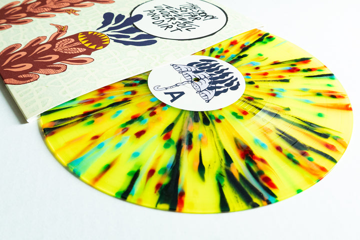 A limited edition yellow vinyl with red, green, and black rainbow splatter by The Story So Far sits partly outside its abstract illustrated cover. Side A is marked by a white label featuring a black umbrella drawing.