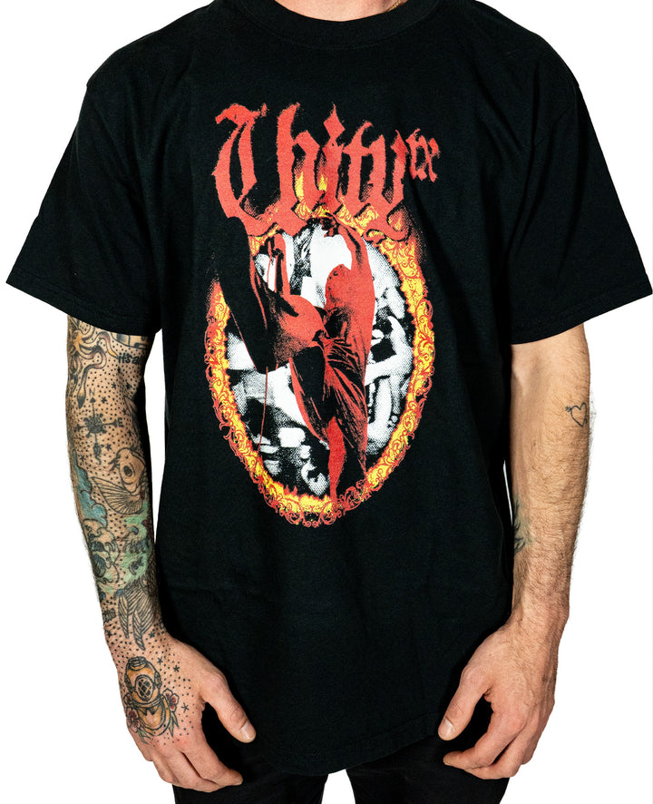 A person in a black UNITYTX Comfort Colors tee with "Unity" in red gothic letters above a fiery ring and red figure stands against a plain white background, showing tattooed arms.