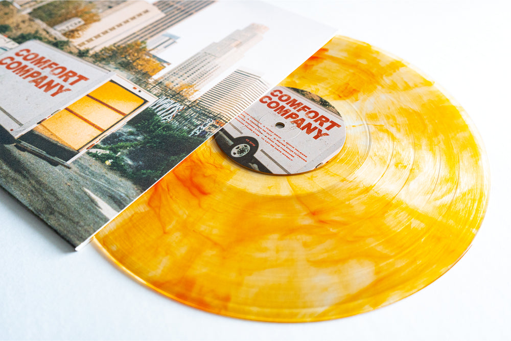 A yellow-orange marble vinyl LP, the Bearings Citrine Deluxe Vinyl, slides from its cover featuring a city moving truck photo. Both label and cover display "COMFORT COMPANY" in bold red. Album presale available.
