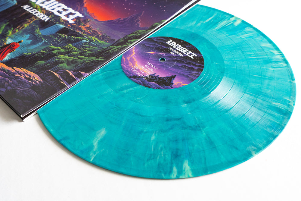A blue marbled Unwell Allegoria Seaside Cove Marble Vinyl LP sits beside its vibrant cover, with fantasy mountains, a river, and glowing pink sky. The record’s label matches the artwork. Now available for album presale.