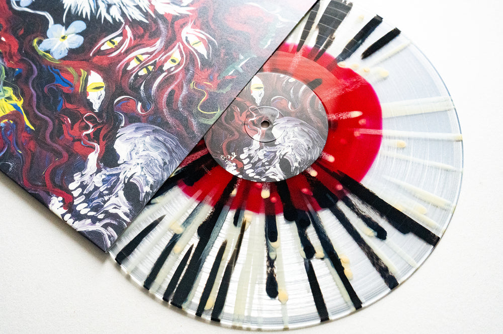A clear splatter vinyl with black and red patterns partially slides out of a sleeve featuring surreal faces and flowing red, white shapes. A striking Mugshot Album Release 2025 collectible.