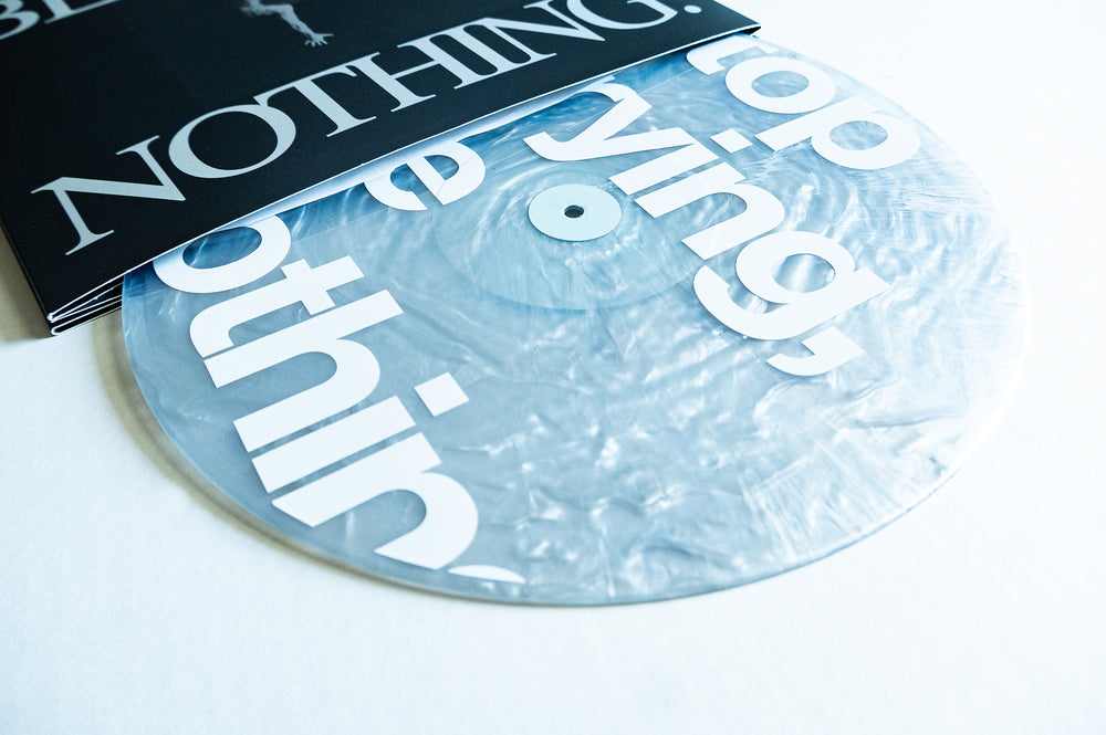A marbled white Boston Manor Be Nothing vinyl record is partially pulled out from a black and white sleeve with bold lettering that reads NOTHING. The record features large white letters and a shiny, textured finish, commemorating the 10 Year Anniversary of Boston Manor’s Be Nothing.