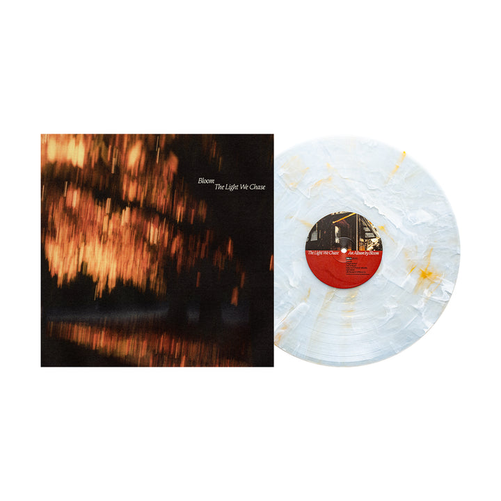 A Bloom Golden Pearl Vinyl LP with a cloudy white and gold design rests by its album cover, showing blurred golden lights on water. The album title "The Light We Chase" and brand name Bloom are displayed.