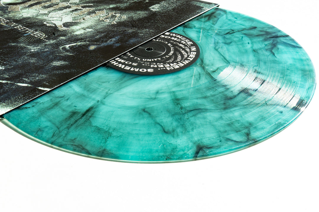 A turquoise and black marbled Electric Smoke Vinyl from UNITYTX’s Somewhere In Between album partially slides out of a dark cover, lying flat on a white surface.