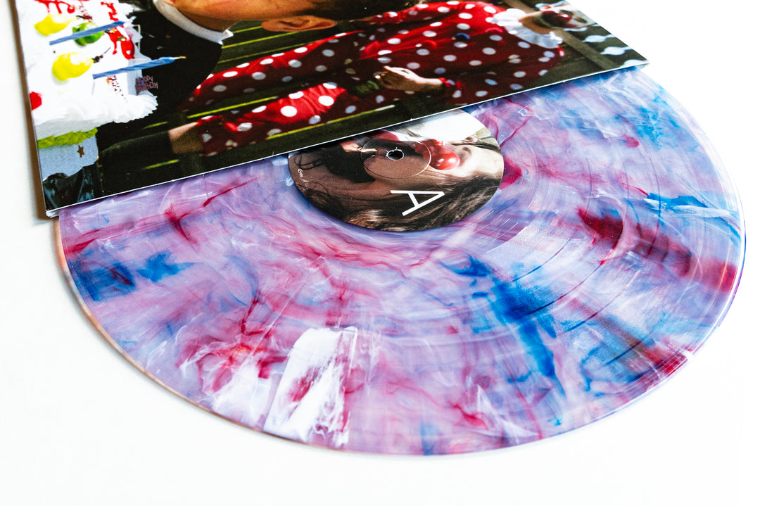A Marble Vinyl LP with purple, pink, blue, and white swirls is partially pulled from a vibrant album cover featuring a close-up of someone in sunglasses and red polka-dot clothing. Perfect for your Album Presale collection from Drug Church.