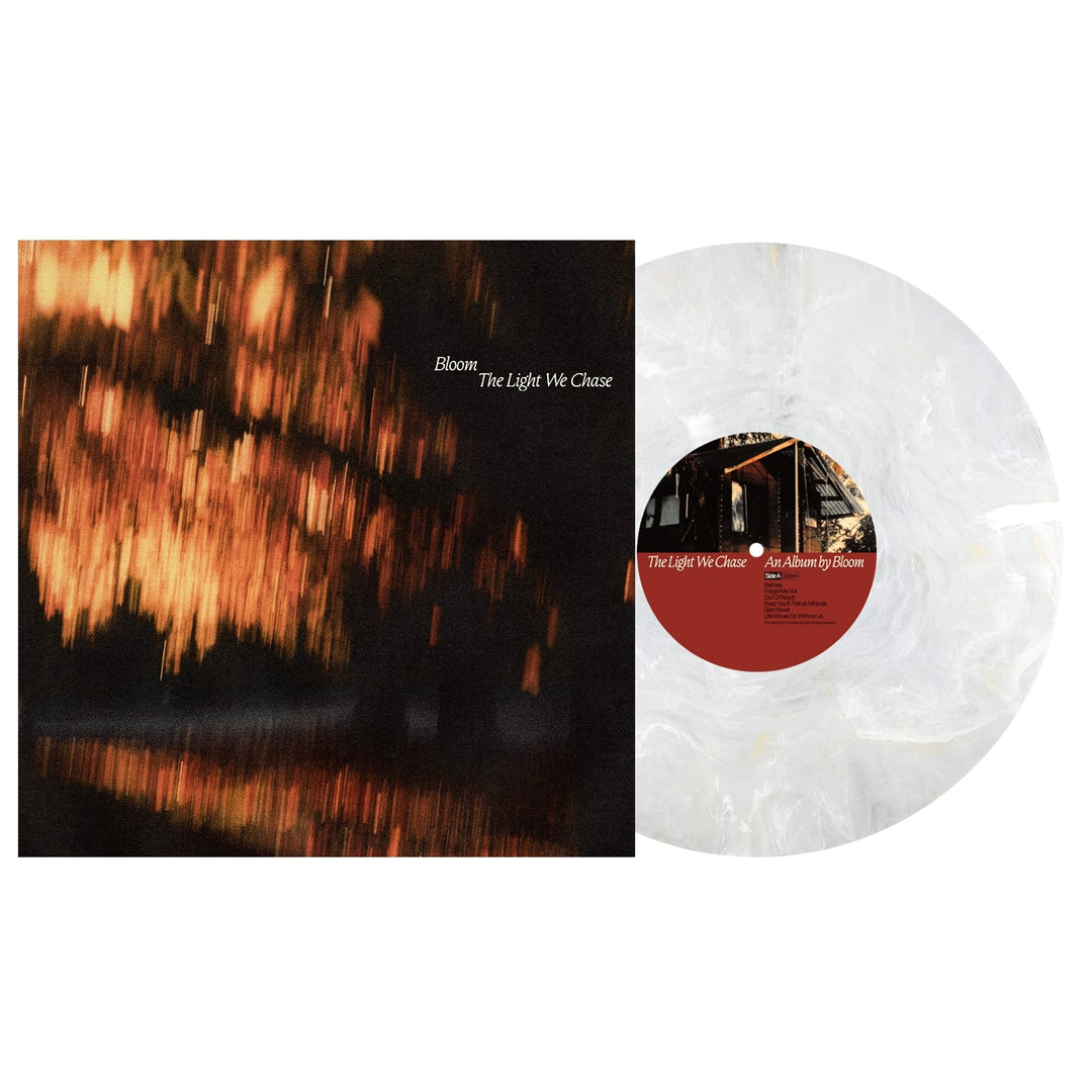 A white marbled vinyl LP, called Golden Pearl Vinyl by Bloom, rests beside its album cover displaying blurred orange and yellow lights on water. The title reads: Bloom - The Light We Chase.