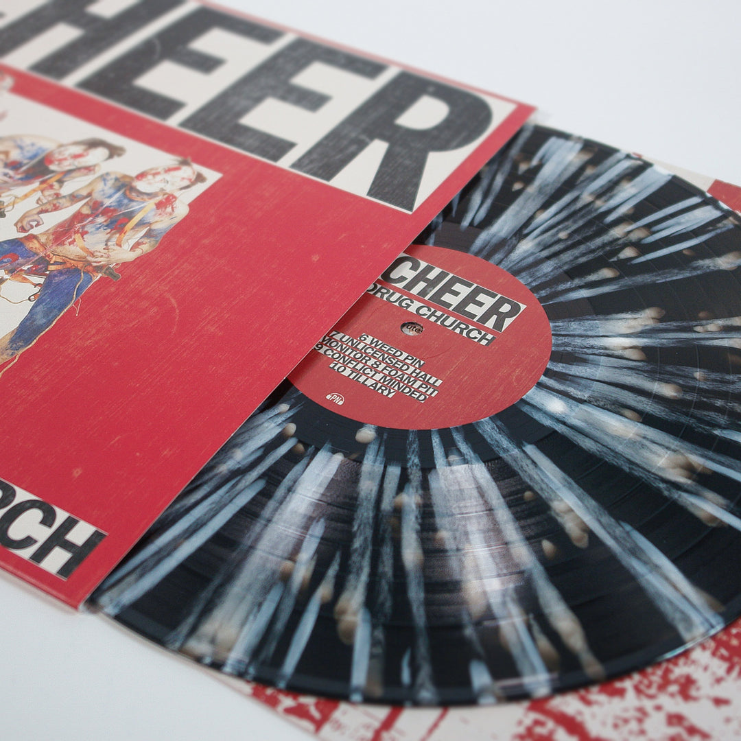 A limited edition black and white splatter vinyl by Drug Church, partially pulled from a red cover with bold CHEER text. Both the record and cover showcase artistic designs and stylized illustrations inspired by Black Ice.
