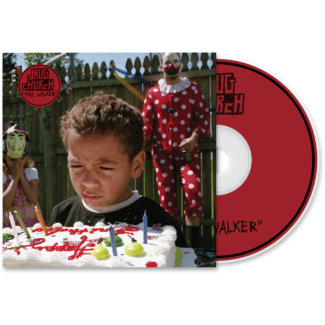 A young boy looks upset before a birthday cake with lit candles, watched by a masked child and an adult clown in the backyard—featured on the unique Drug Church album cover.