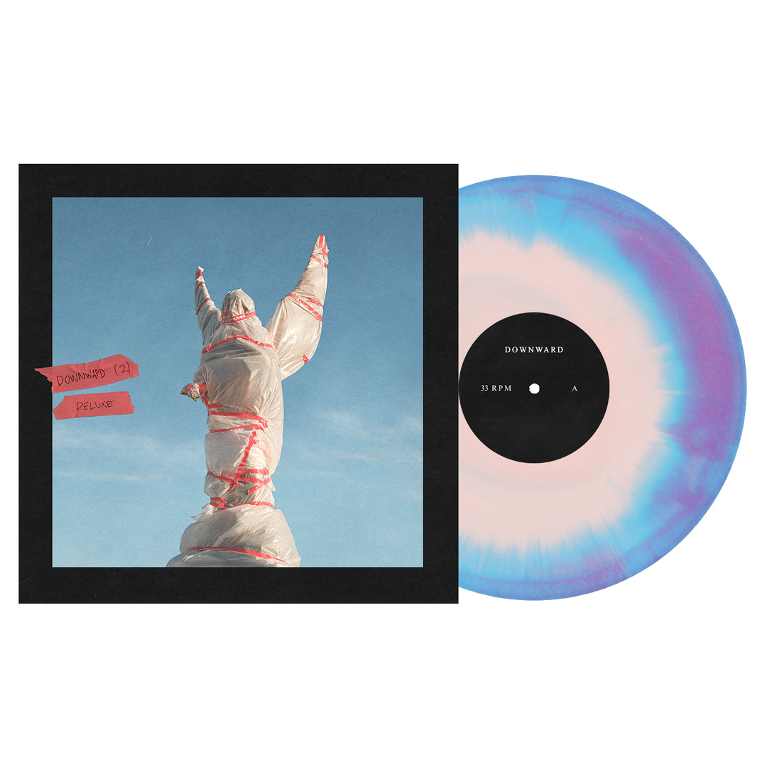 Square album cover featuring a statue wrapped in plastic and red tape, arms raised against a blue sky. Beside it is the DOWNWARD Deluxe Baby Pink/Cyan Blue/Deep Purple vinyl LP, now available for presale.