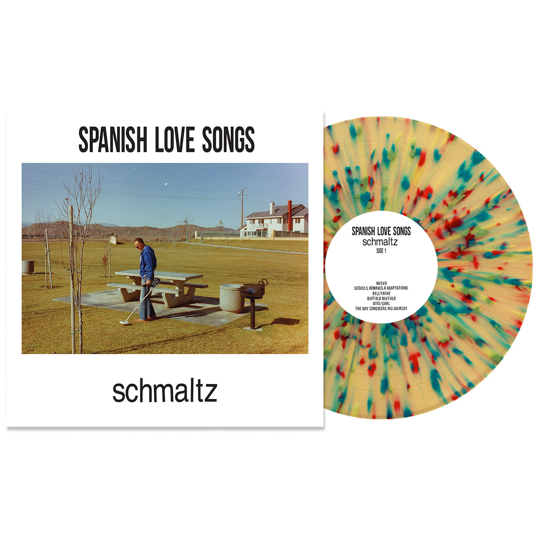 The Spanish Love Songs album "Schmaltz" is displayed with cover art of a person by a picnic table in a grassy park. The cream Vinyl LP, called Rainbow Splatter Vinyl, features red, blue, and yellow splatter effects.