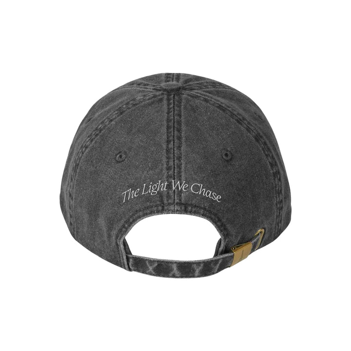 Back view of a faded black Bloom Death Moth Hat with The Light We Chase embroidered in white above the adjustable strap and brass buckle.
