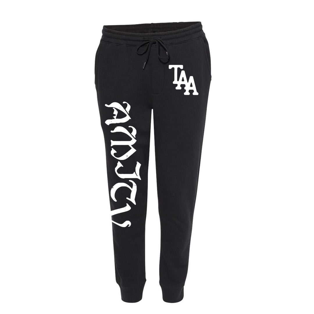 Black midweight fleece sweatpants by The Amity Affliction, featuring a drawstring waist, cuffed ankles, TAA in white on the right hip, and a large white vertical script along the left leg.