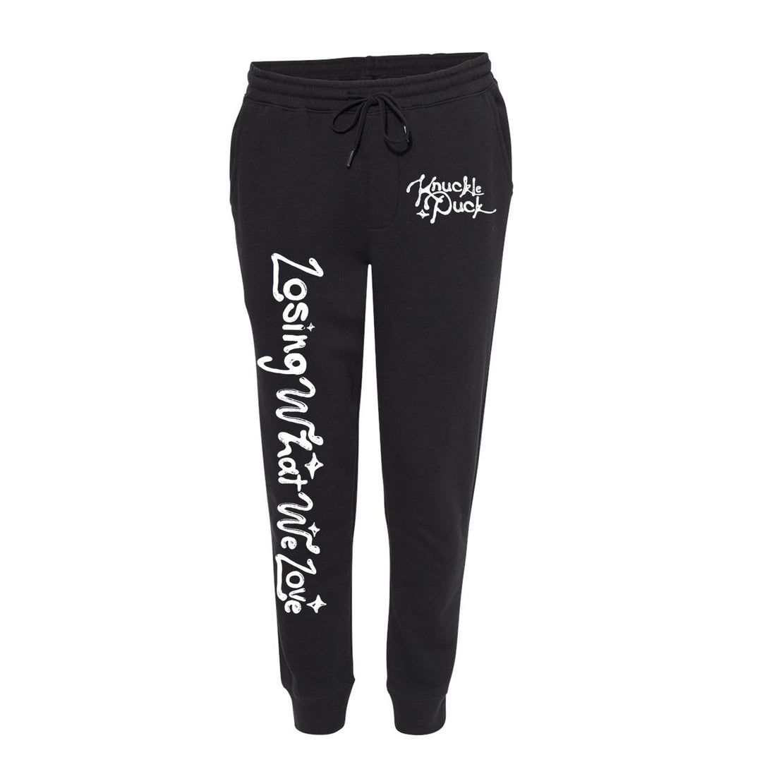 Black fleece sweatpants by Knuckle Puck with a drawstring waist, "Losing What We Love" in large white script down the left leg, and Knuckle Puck plus star detail on the right pocket area.