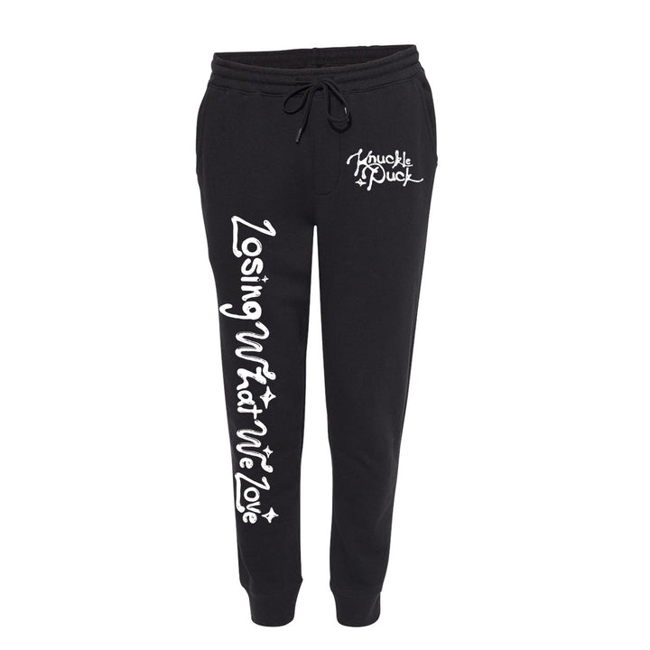 Black fleece sweatpants by Knuckle Puck with a drawstring waist, "Losing What We Love" in large white script down the left leg, and Knuckle Puck plus star detail on the right pocket area.