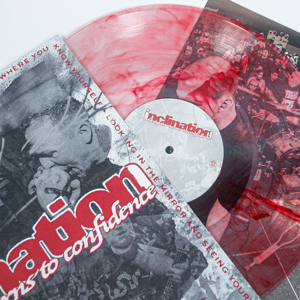 A red and white Bloodshot Marble Vinyl LP by Inclination is partially in its sleeve, which shows a black-and-white live band photo. Inclination and the album title When Fear Turns To Confidence appear in bold red and white text.