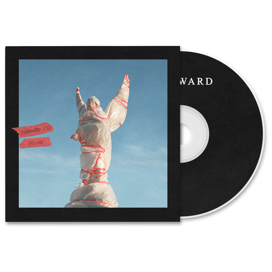 CD case and disc for the Downward Bundle Deluxe CD by DOWNWARD. The cover shows a statue wrapped in plastic and red tape, arms raised against a blue sky. The black disc is labeled DOWNWARD—available now for album presale.