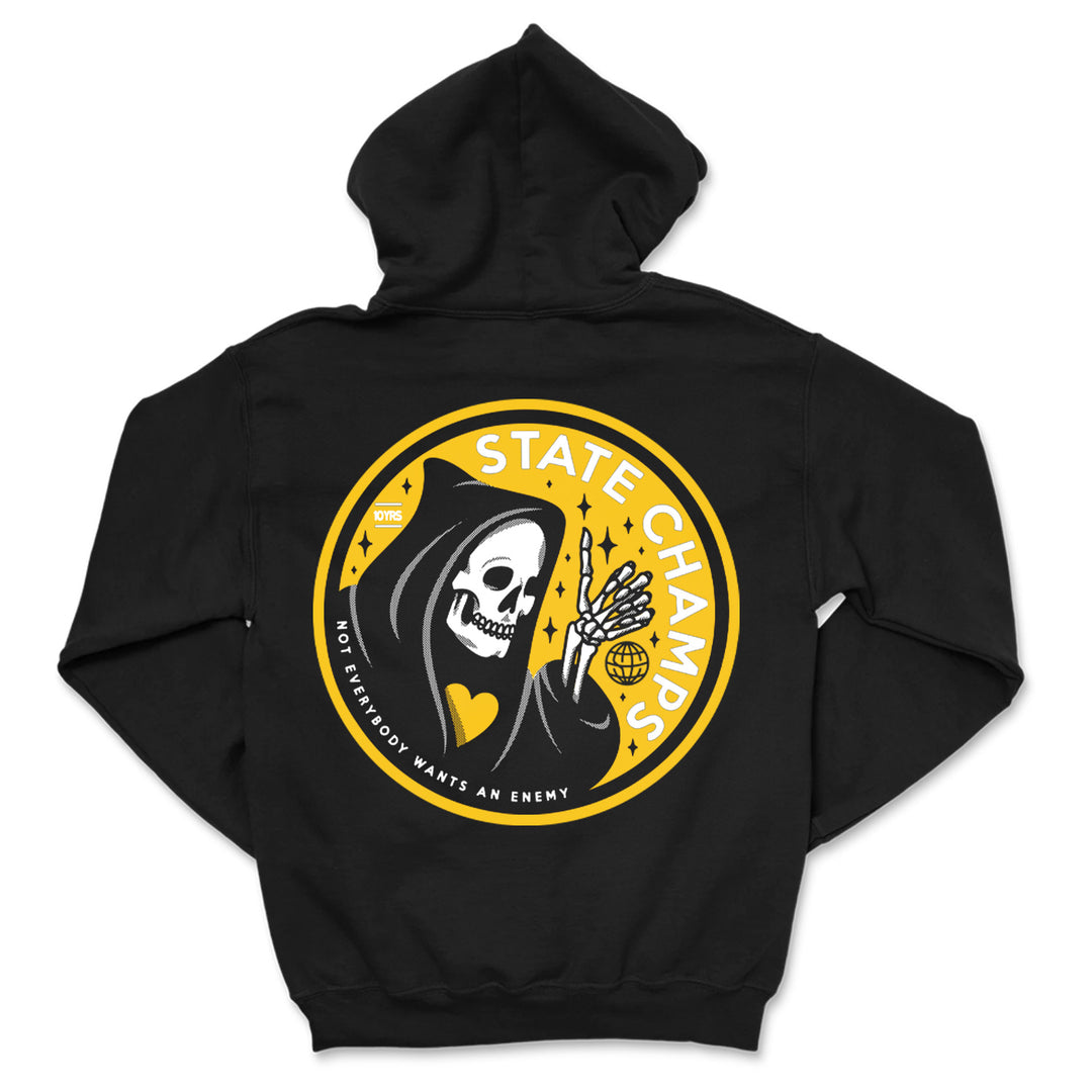 A black State Champs sweatshirt with a circular graphic of a grinning skeleton in a hooded cloak, holding a yellow heart and globe. Text reads: STATE CHAMPS and NOT EVERYBODY WANTS AN ENEMY.