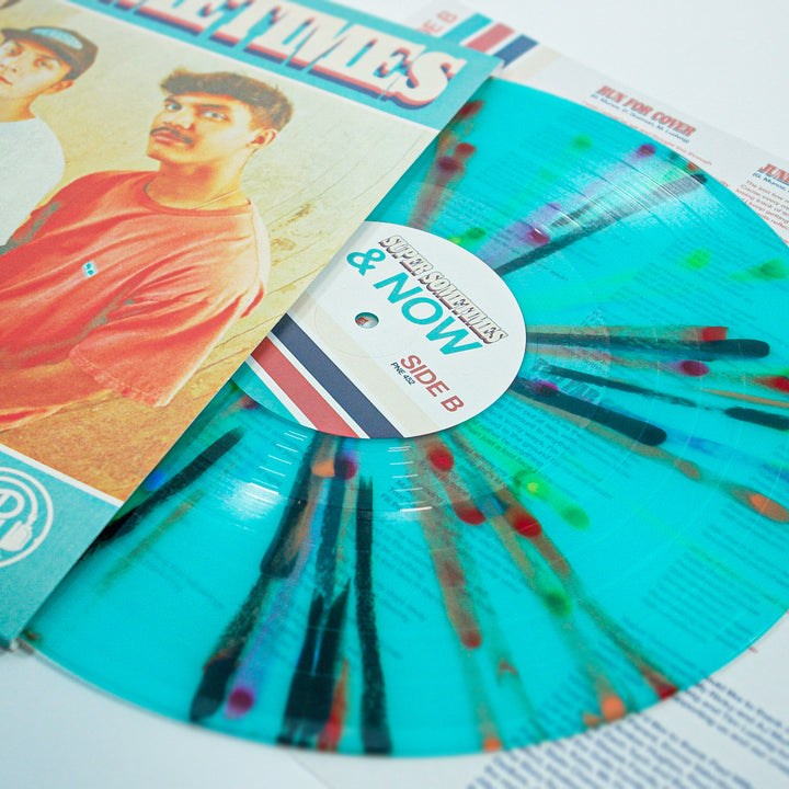 A turquoise vinyl with Rainbow Splatter from Super Sometimes sits partially in its sleeve, which displays a photo of two men and bold "Then & Now" text. The record label shows it’s Side B.