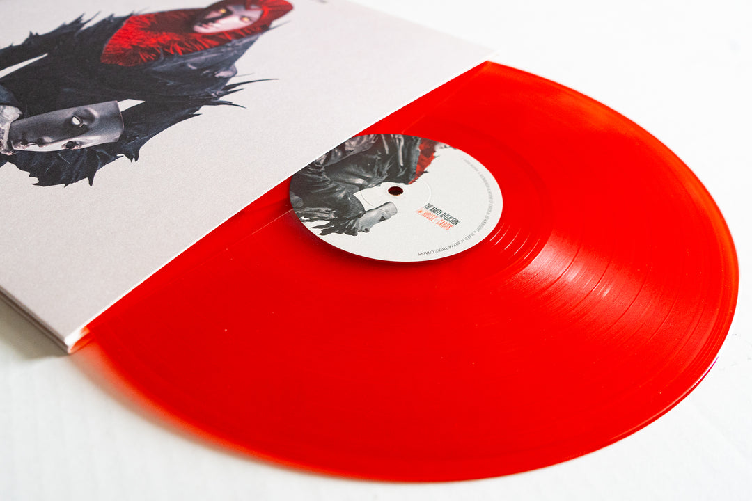 A vivid Blood Red Vinyl LP by The Amity Affliction partially slides out from its album cover, featuring black-and-white portraits with red accents on a white background. The record's label echoes the cover artwork.