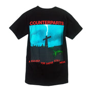 Back of t-shirt has the image of a cross in a field with the word "Counterparts" in red ink over it. 
