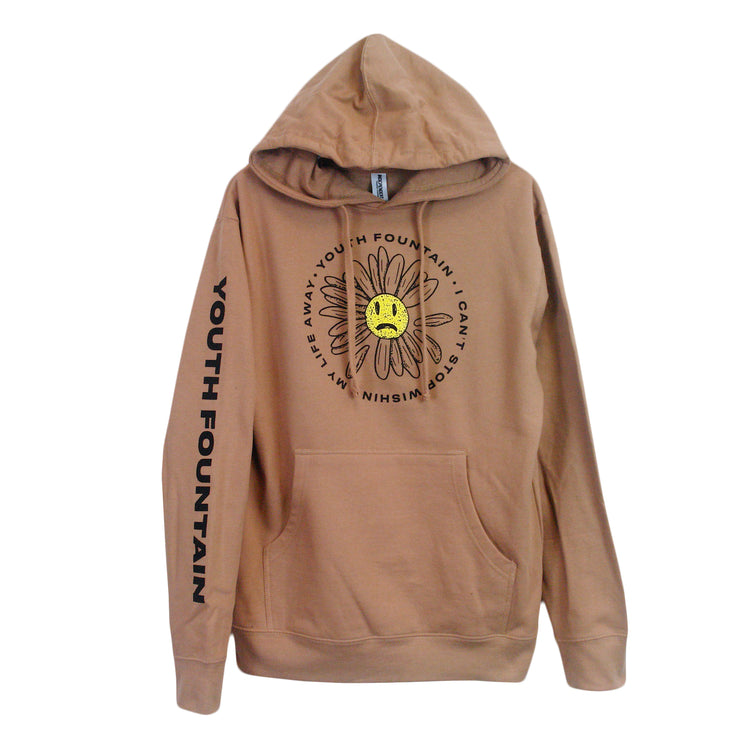 image of a sand colored pullover hooded sweatshirt on a white background. the hoodie has a front and center chest print in black of a circle with text that says youth fountain i can't stop wishing my life away. there is a daisy flower with a yellow sad face in the center on the the text circle. on the left sleeve going down in black print says youth fountain