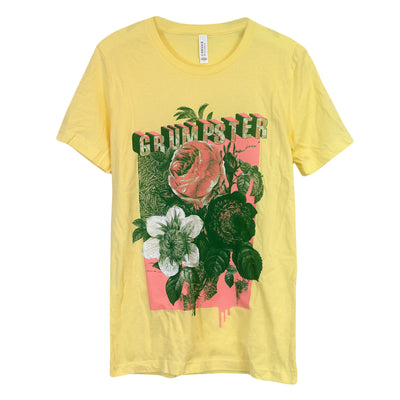 Image of a yellow tee shirt on a white background. Tee reads "Grumpster" by the collar above a design of 3 flowers. One flower is pink, one flower is white, and the last flower being mostly green. 