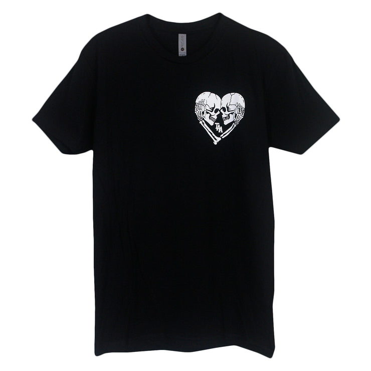 image of the front of a black tee shirt on a white background.  The left chest has a white colored graphic of two skeleton heads looking at each other closely. One skeleton reaches their hand to hold the side of the head of the others, which creates a heart shaped image